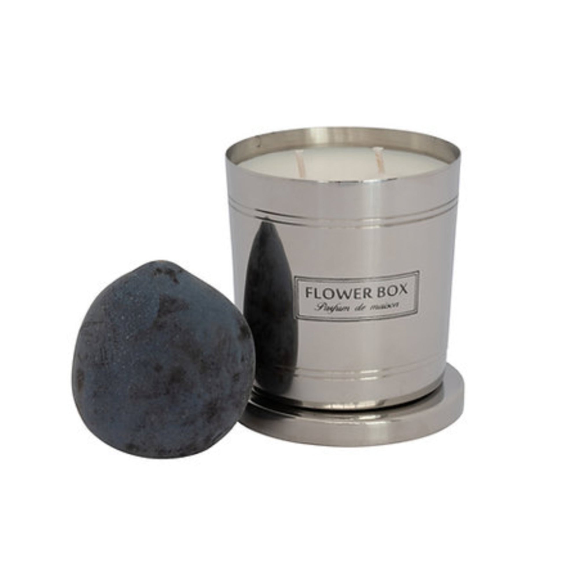 Image of a silver, brushed metal candle container with three wicks and a matching circular base. A rectangular label with black text on a white background reads "FLOWER BOX Pufum de maison". In front of the candle is a plum. The background is white.